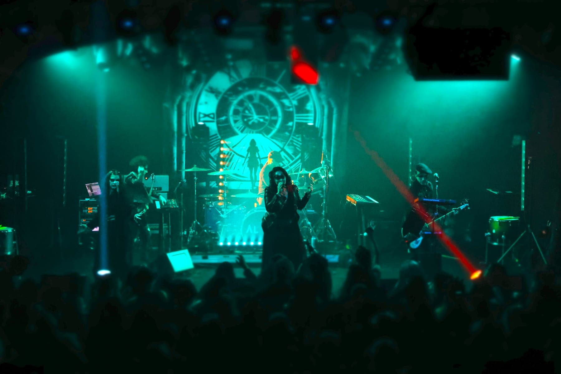 AL1CE performing live under teal stage light in front of the clock backdrop