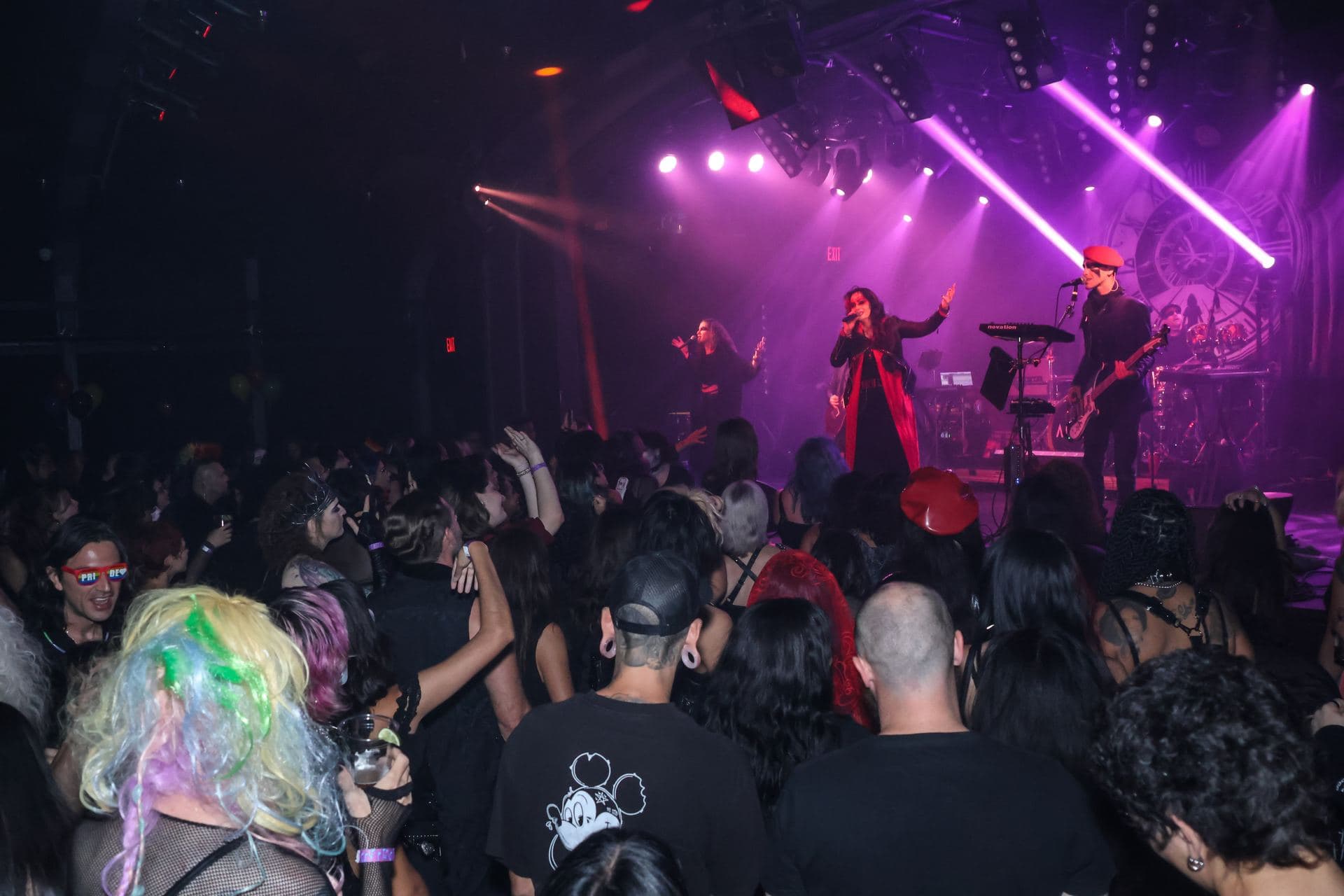 A packed crowd on the floor with AL1CE performing under violet light behind them