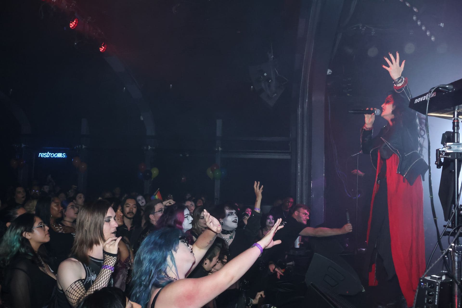 Hands raised in the front row as the AL1CE vocalist leans out over the crowd in a red coat
