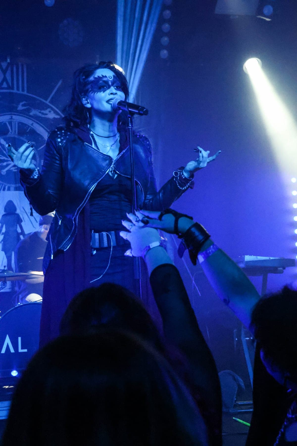 AL1CE vocalist on stage under blue light with the clock backdrop behind her